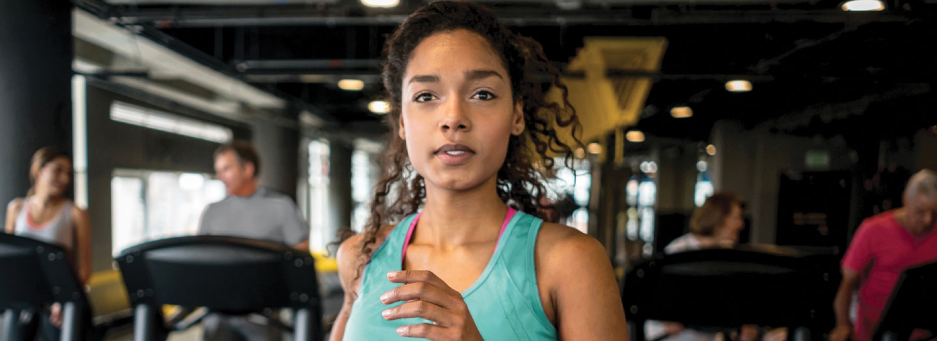 Woman in green tank top running on treadmill at gym