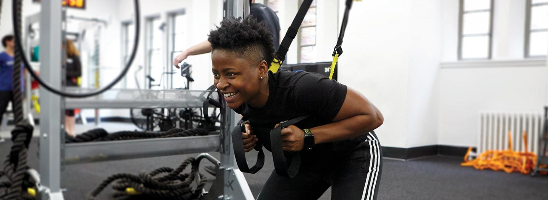 Instructor demonstrates a squat with TRX equipment in fitness class at YMCA gym