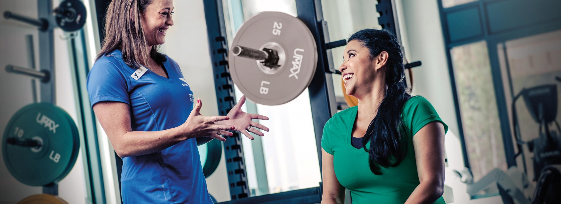 YMCA personal trainer smiling and laughing with fitness client in front of weight lifting rack machine at gym