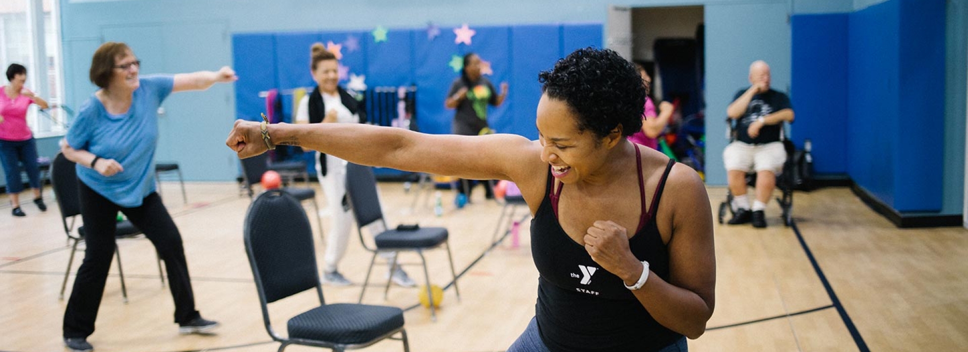 YMCA fitness instructor smiles while leading chair yoga class in basketball court of Ridgewood YMCA