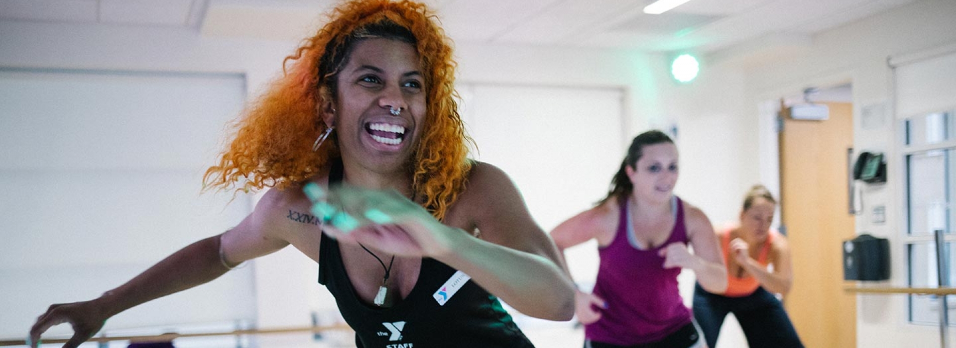 YMCA zumba instructor smiling while swinging her arms and leading class in fitness studio at Ridgewood YMCA