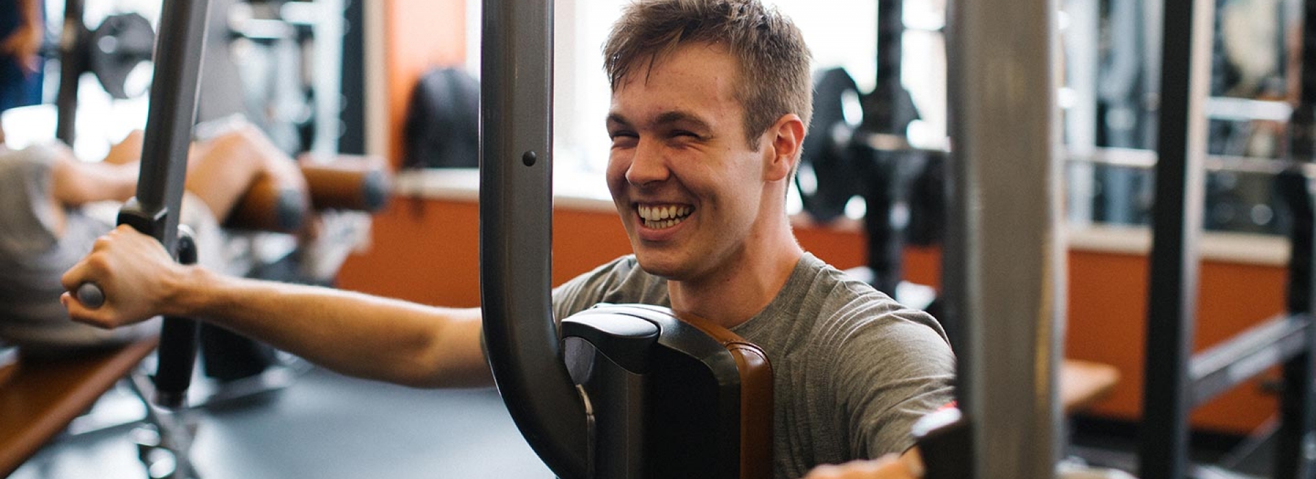 Man grins while using strength training machine for arms at Ridgewood YMCA fitness center