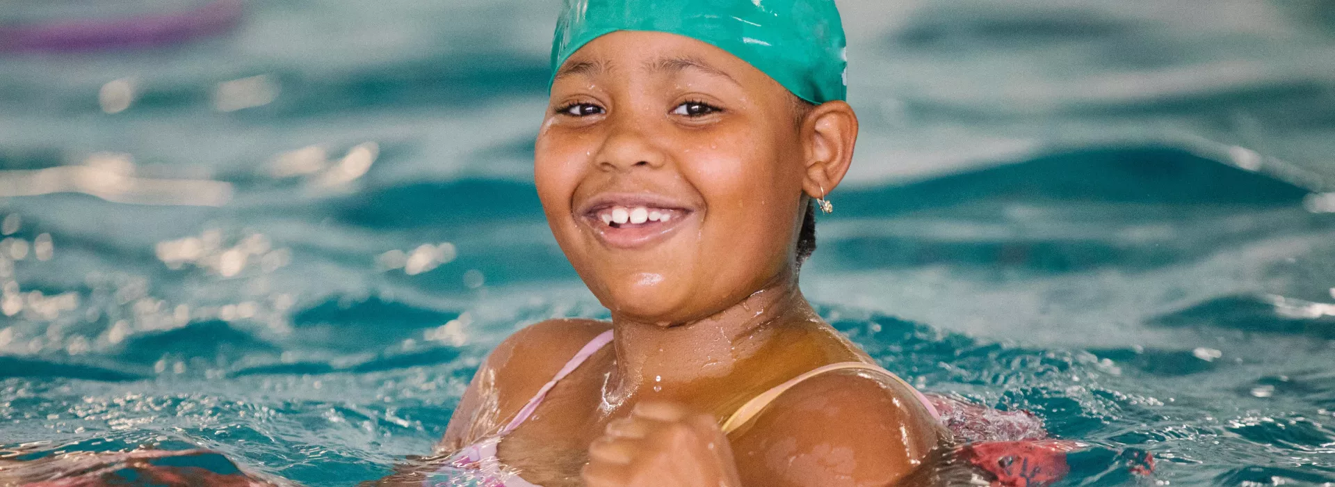 Young girl smiles while swimming in YMCA indoor pool in Castle Hill, Bronx