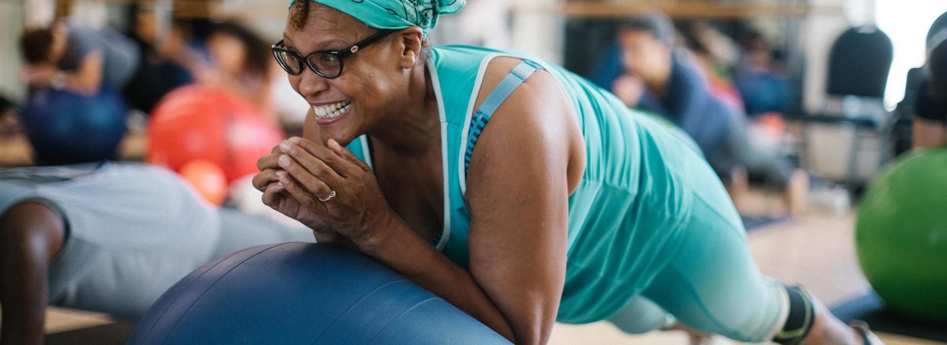 Woman with aqua bandana smiles while doing core exercises during Rockaway YMCA pilates mat class