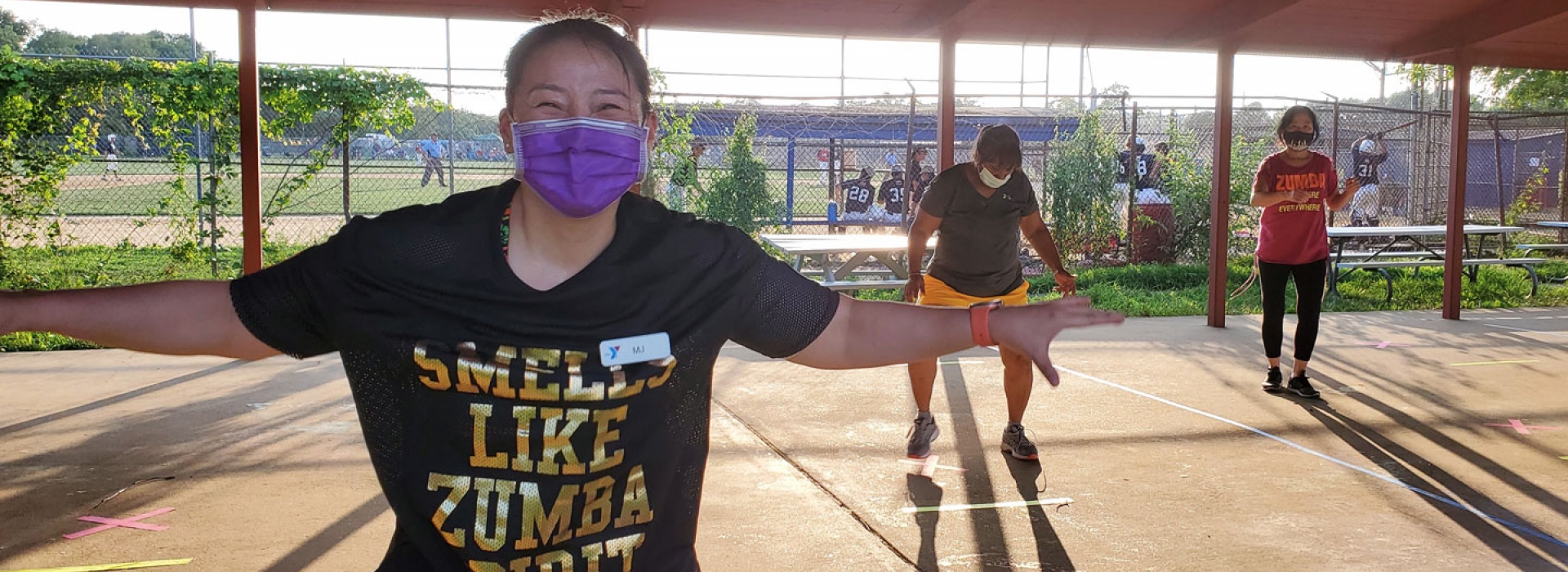 A Zumba instructor smiles and dances at an outdoor fitness class at the YMCA.