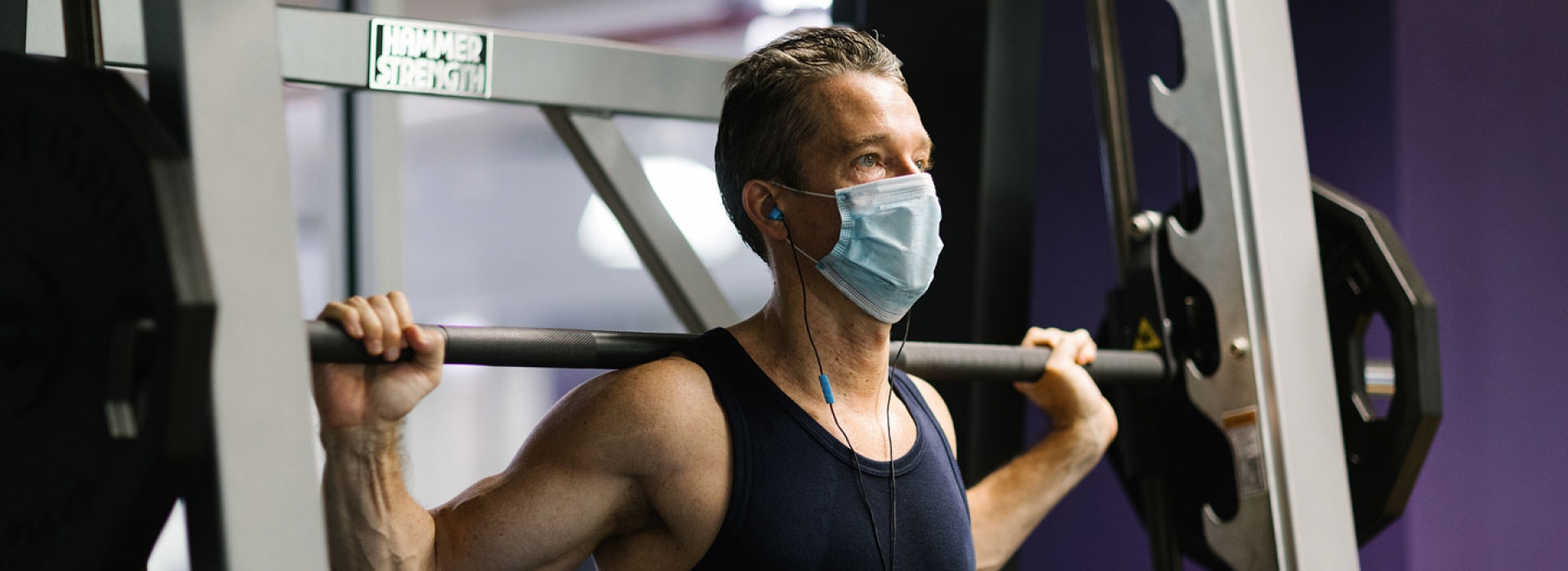A YMCA member in a mask lifts weights.