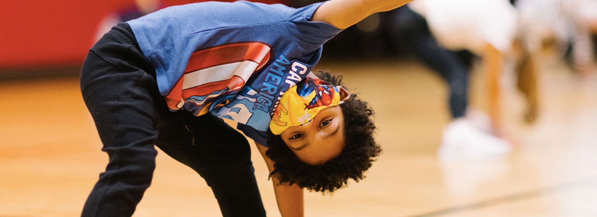 A boy wearing a mask does a yoga pose at the YMCA.