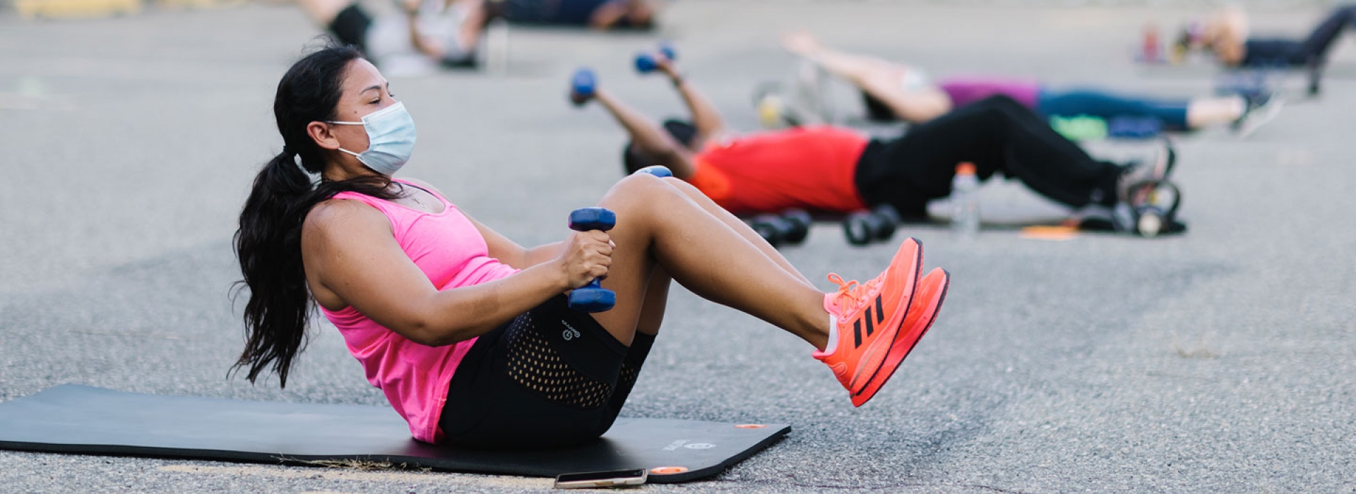 A woman in a mask works out with free weights outdoors at the YMCA.