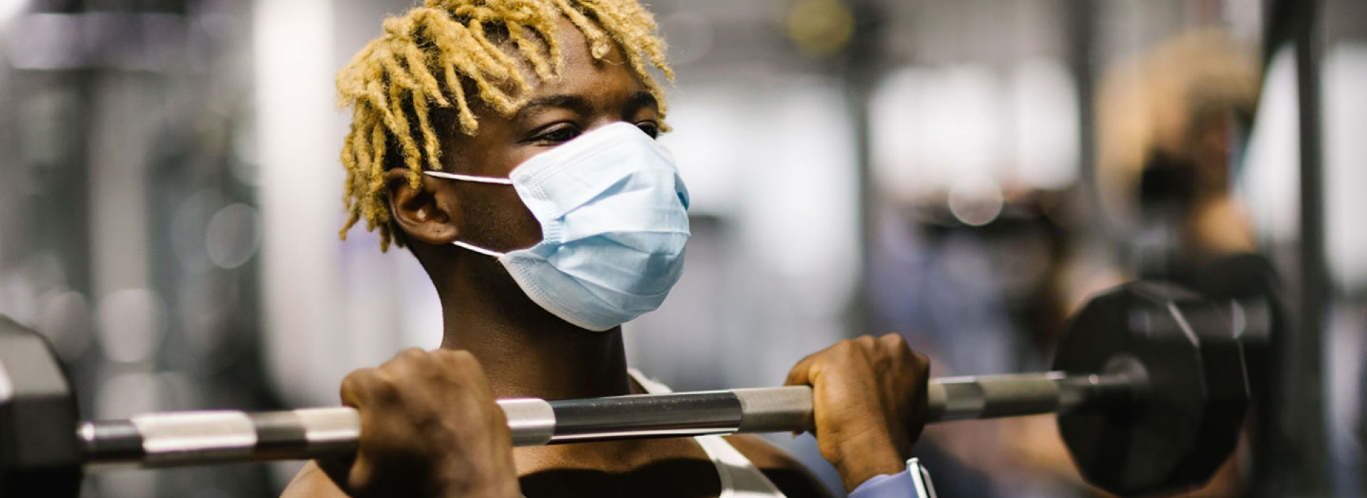 A man in a mask works out by lifting weights at the YMCA.