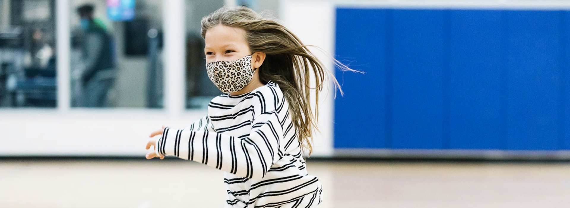 A girl runs in a large gym during a YMCA camp or learning lab.