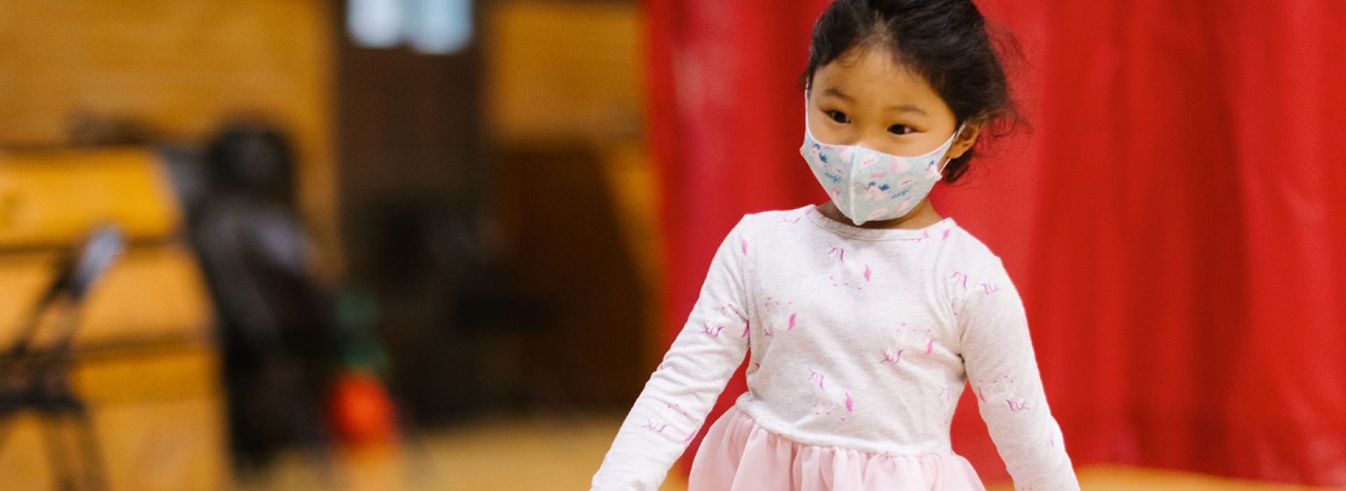 A girl in a mask and a pink ballet dress at the YMCA.