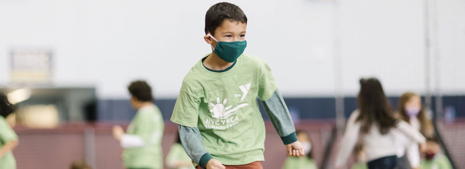 A boy in a mask smiles during camp at the YMCA.