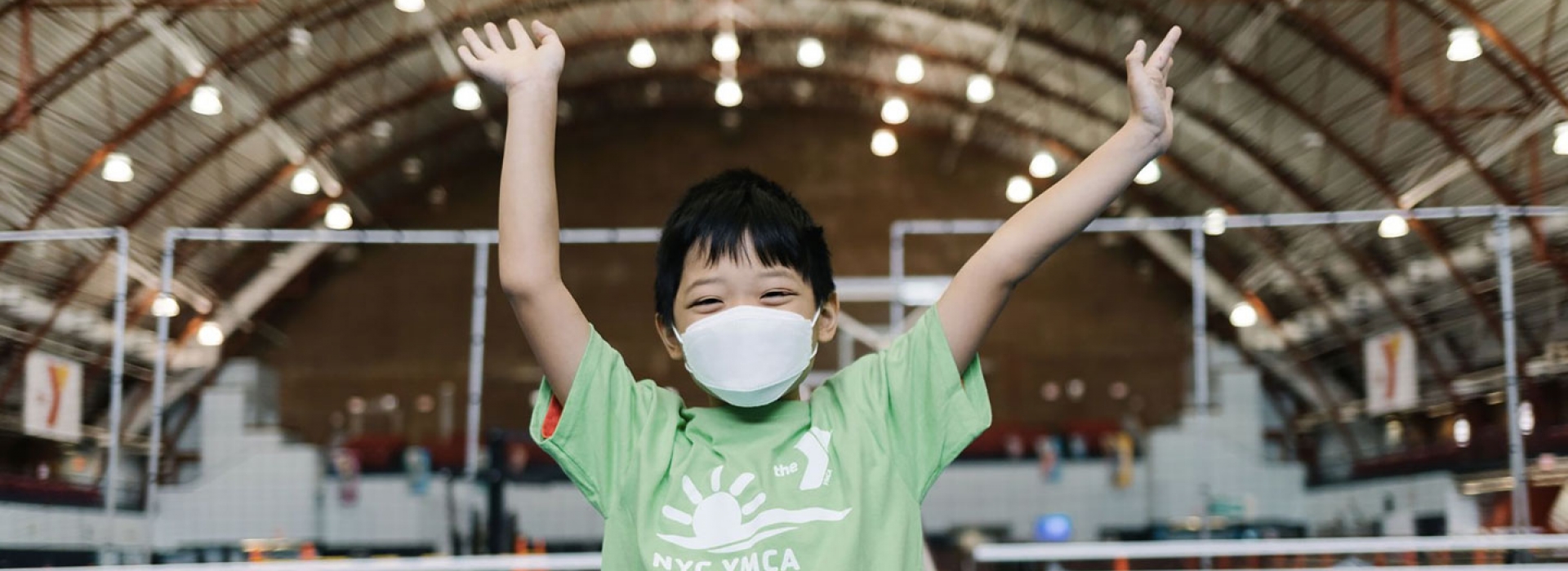 A boy in a mask smiling and waving during camp at the YMCA.