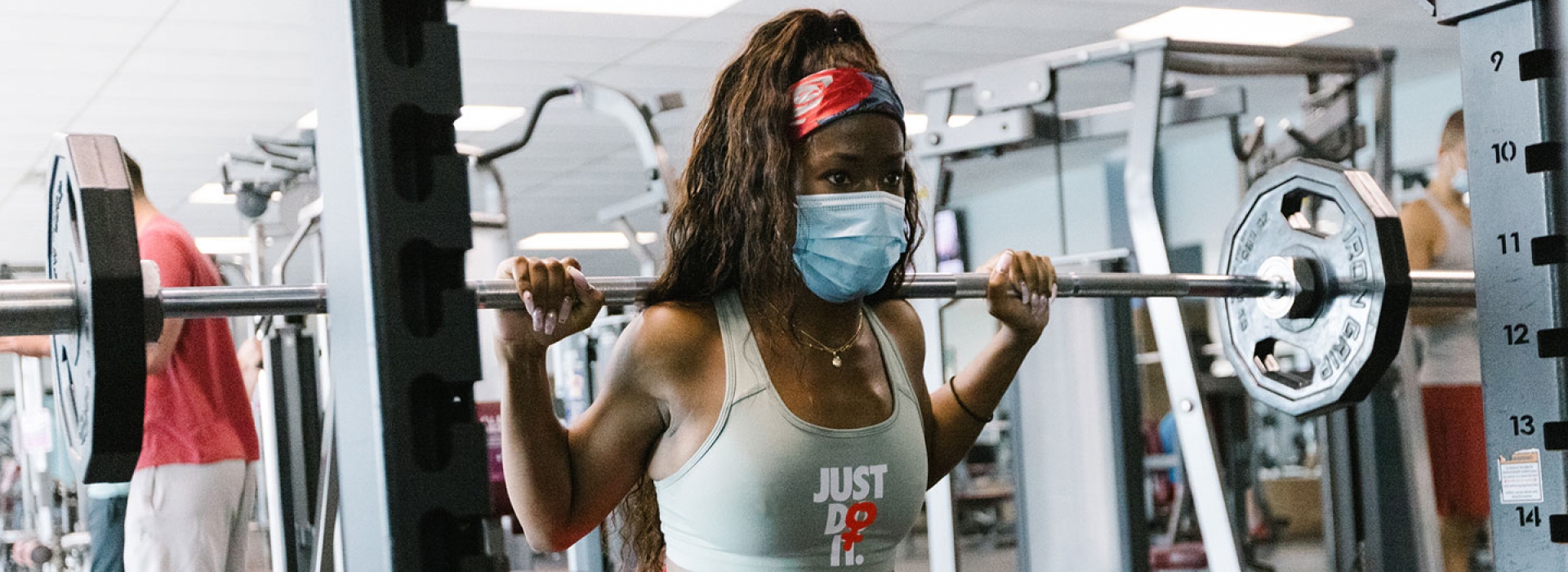 A woman in a mask lifts weights at the YMCA.