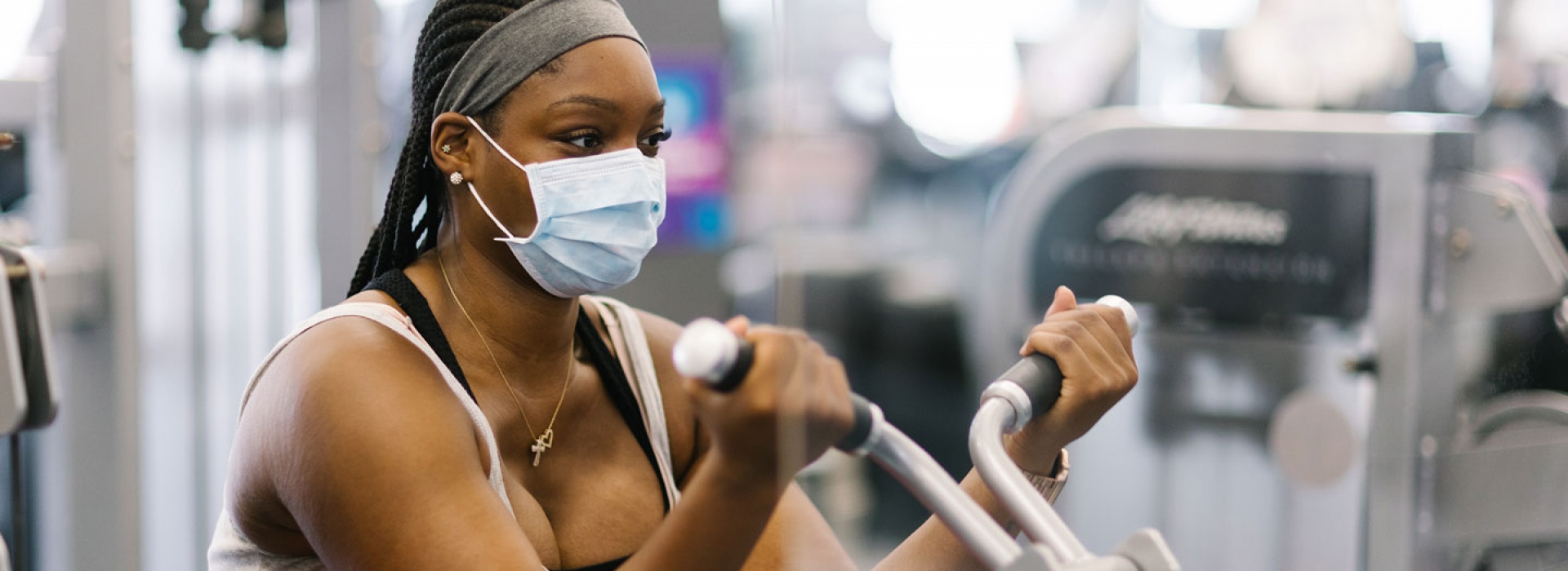 A woman in a mask does strength training at the YMCA.