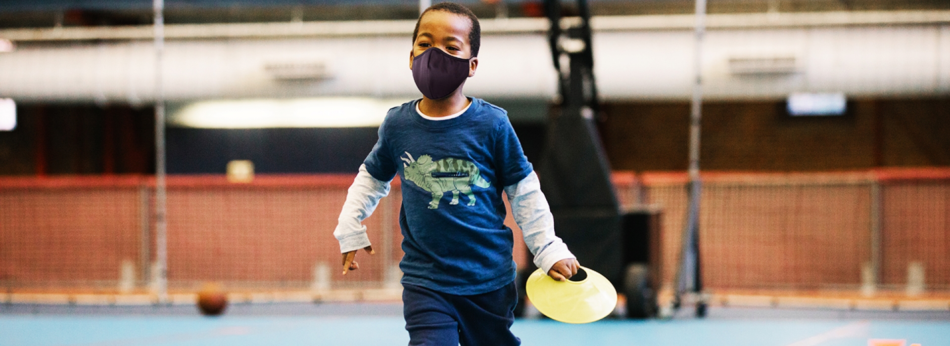 A boy in a mask running inside a YMCA gym