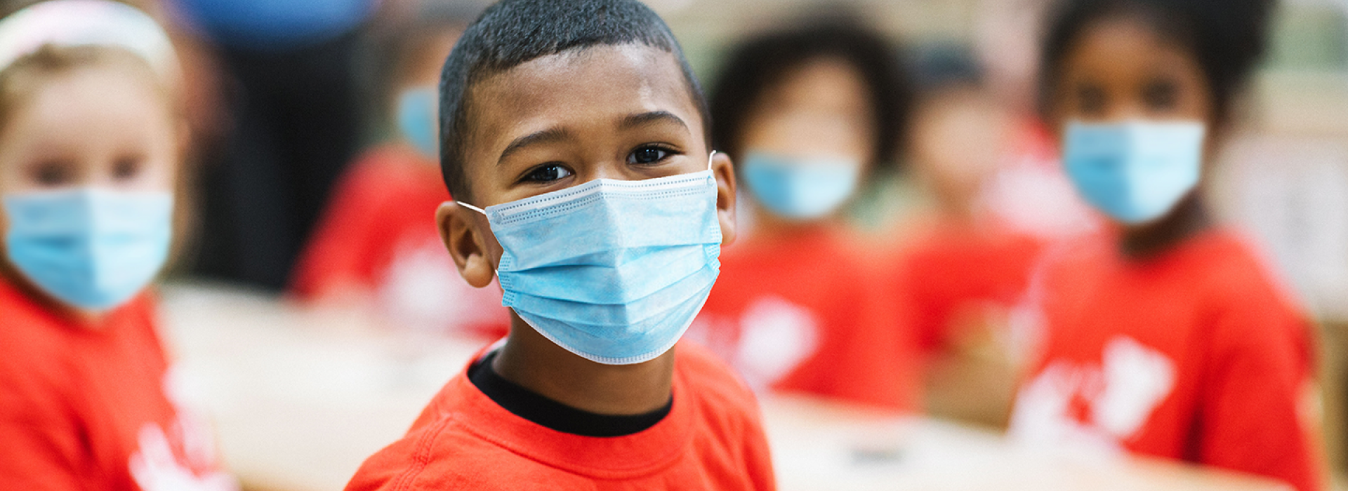 A boy in a mask sitting and smiling at Y Camp