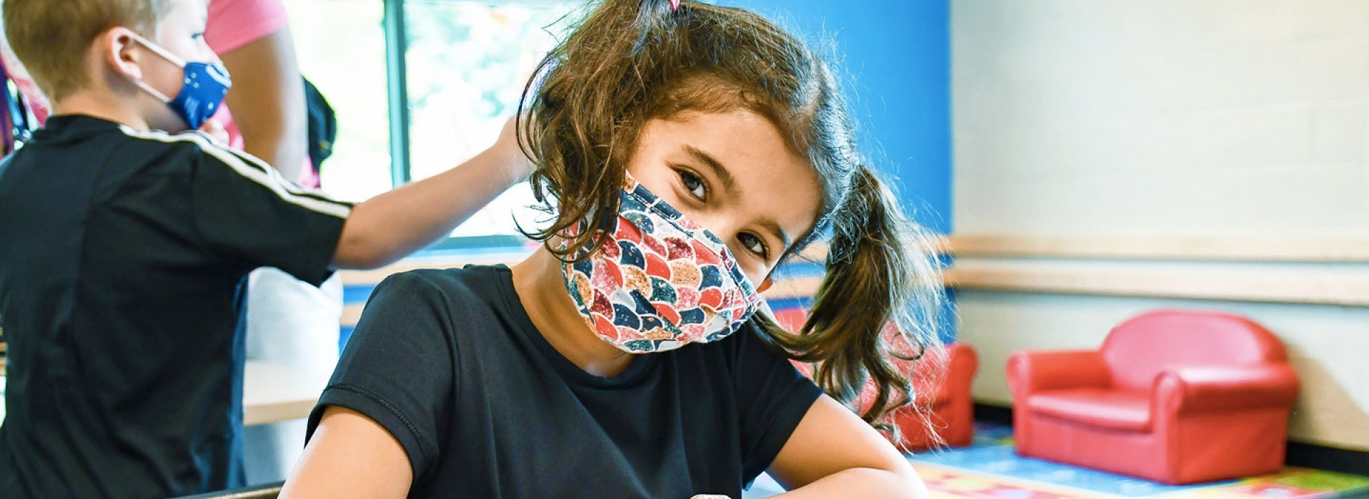 A girl in a mask smiles at a YMCA camp.
