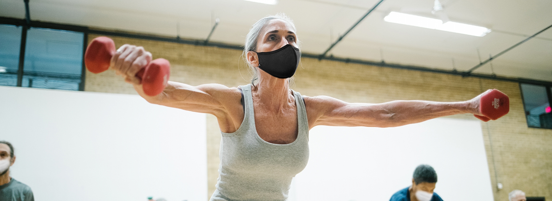 A woman wearing a mask lifting weights in a group exercise class