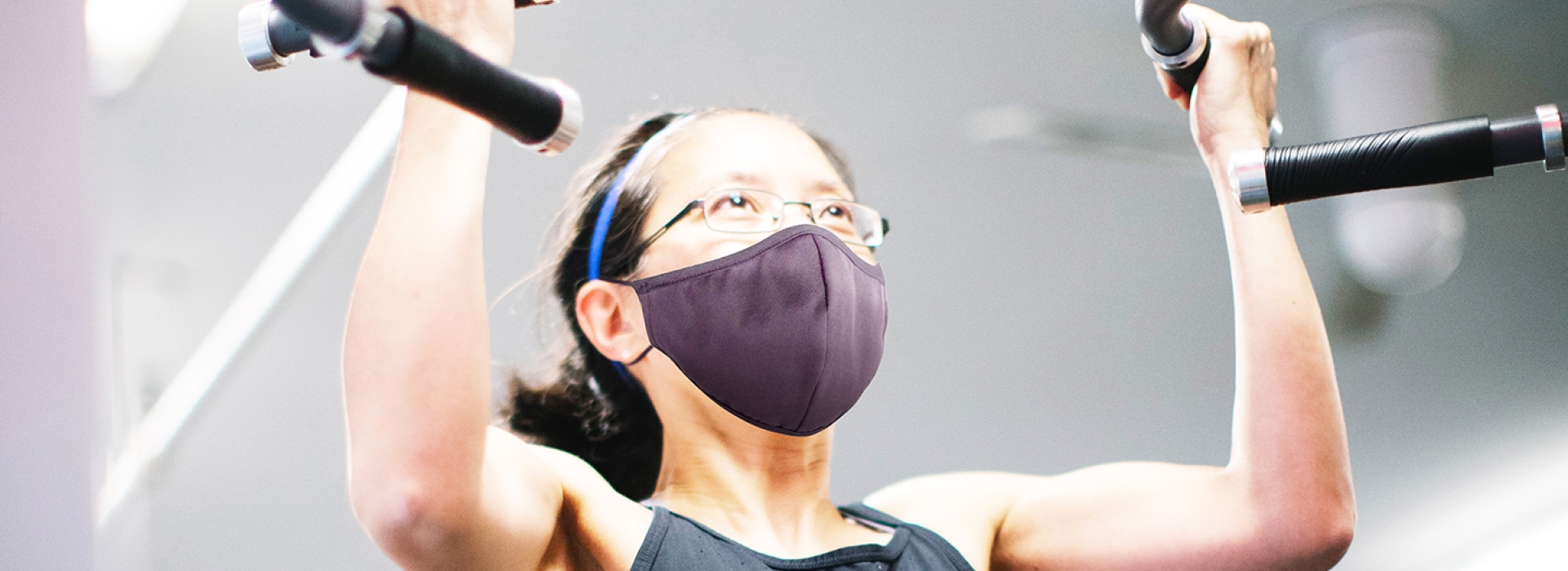 A woman wearing a mask doing a pull up on workout equipment